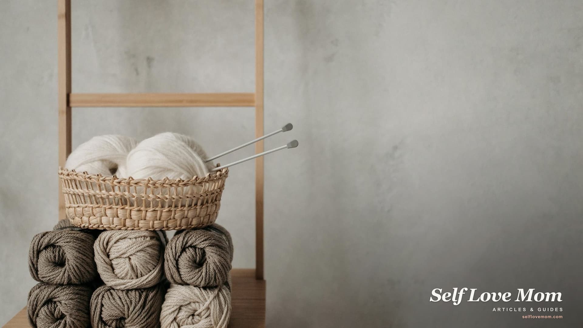 A woven basket of yarn rolls and knitting tools on a wooden table in soft natural light, a quiet hobby setup for a stay-at-home mom.