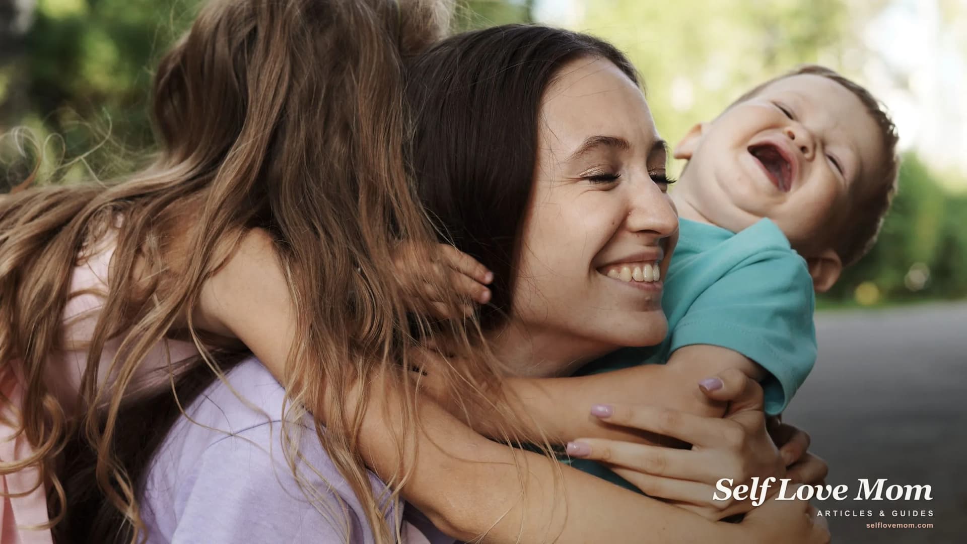 A mother laughs outdoors as her two children hug her close, the warmth at the center of family life.