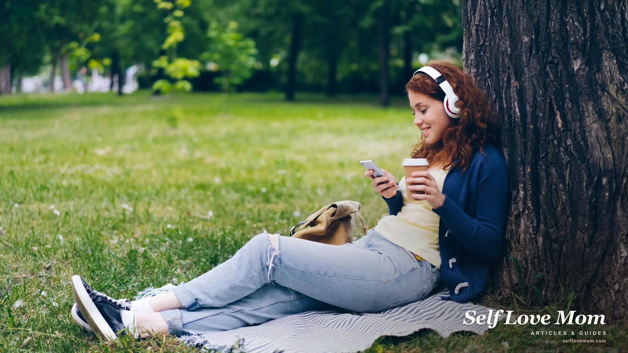 A smiling mom in headphones holds her phone and coffee in a park, taking a self-care break with a free app.