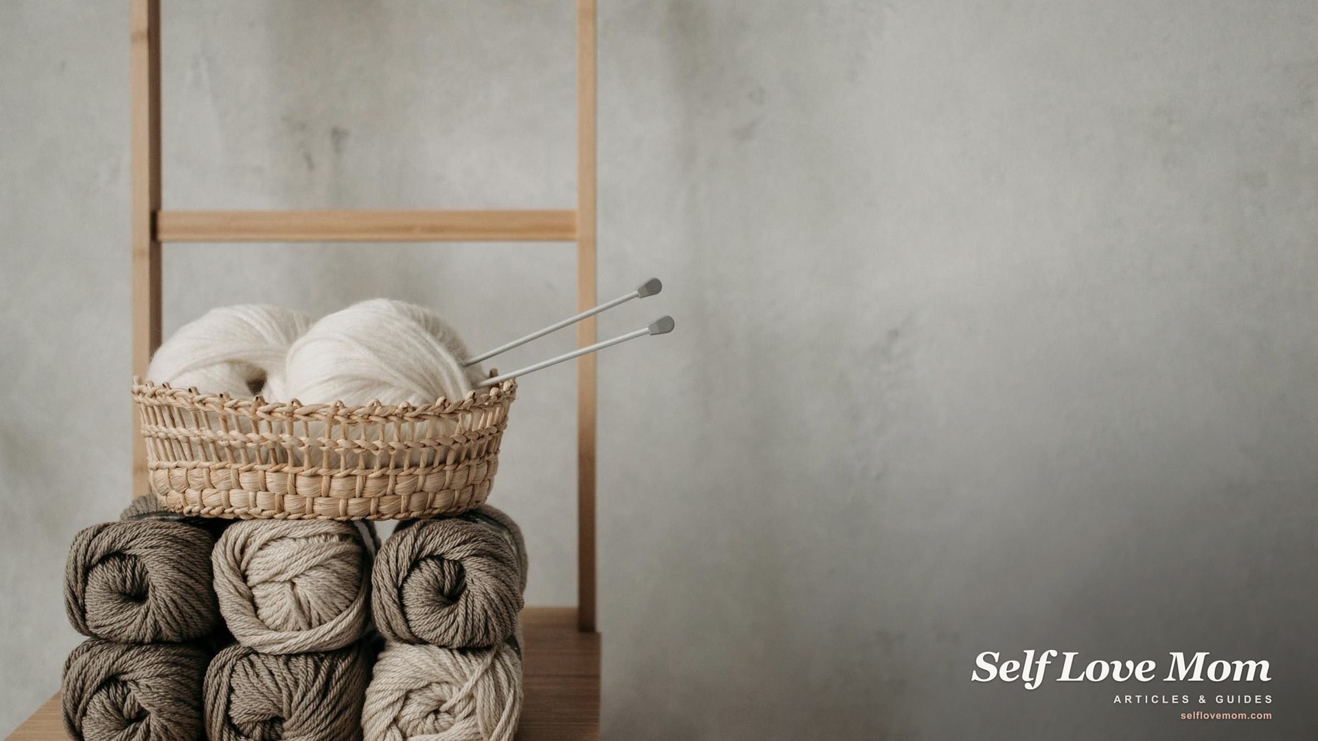 A woven basket of yarn rolls and knitting tools on a wooden table in soft natural light, a quiet hobby setup for a stay-at-home mom.