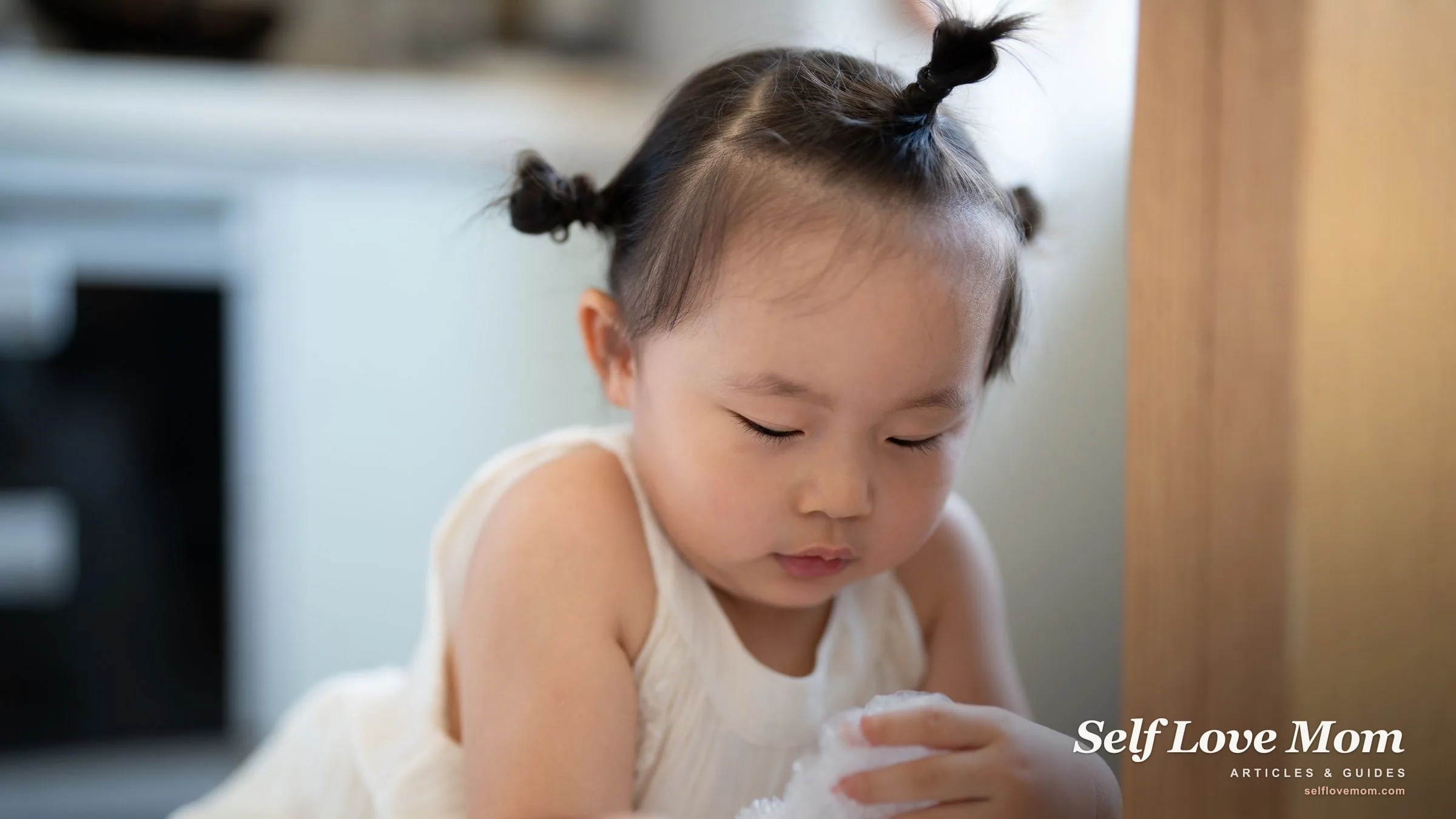 A toddler girl focuses on hands-on play indoors in a bright home.