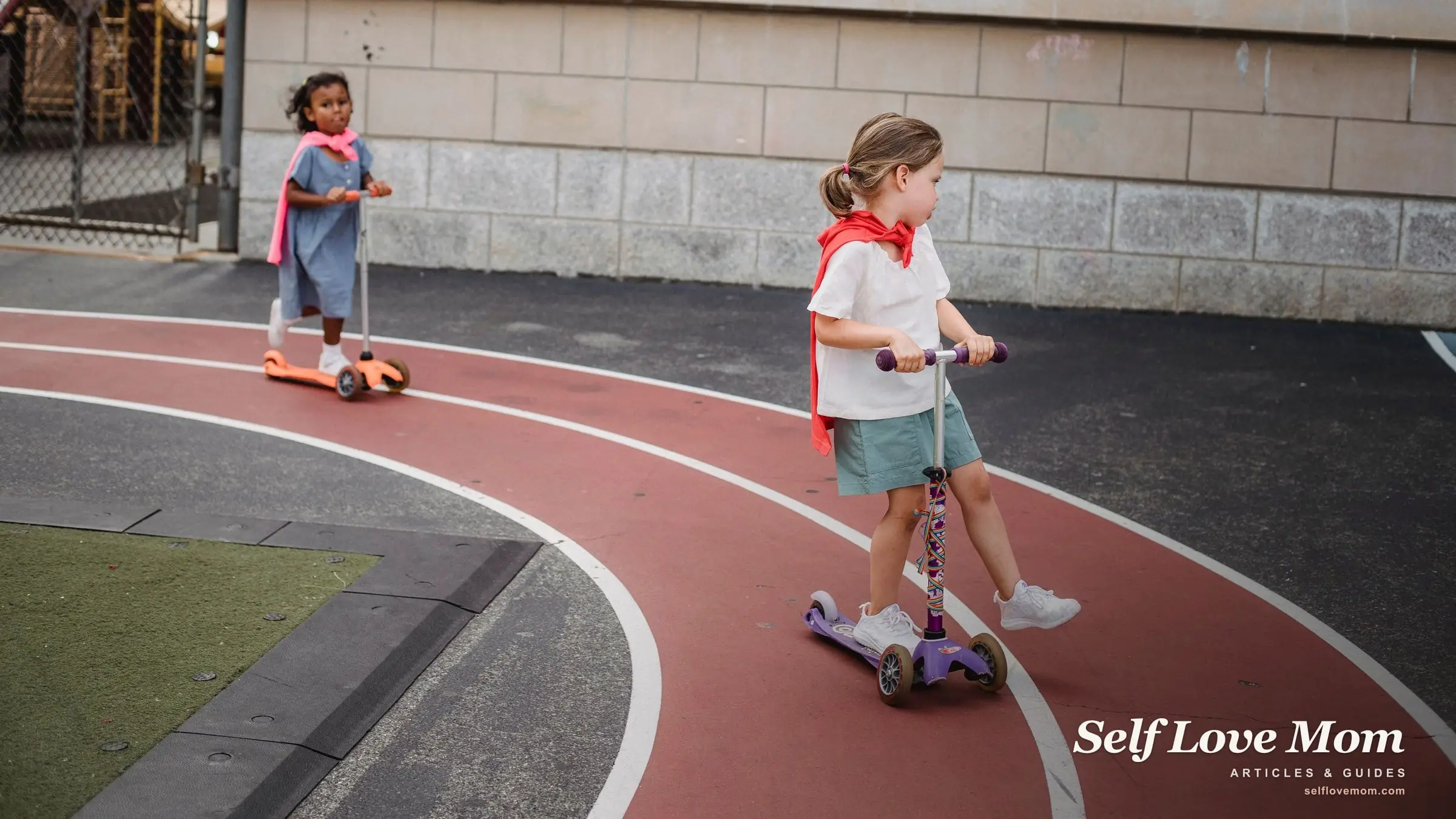 Two preschool girls in red capes ride scooters on an outdoor playground court.