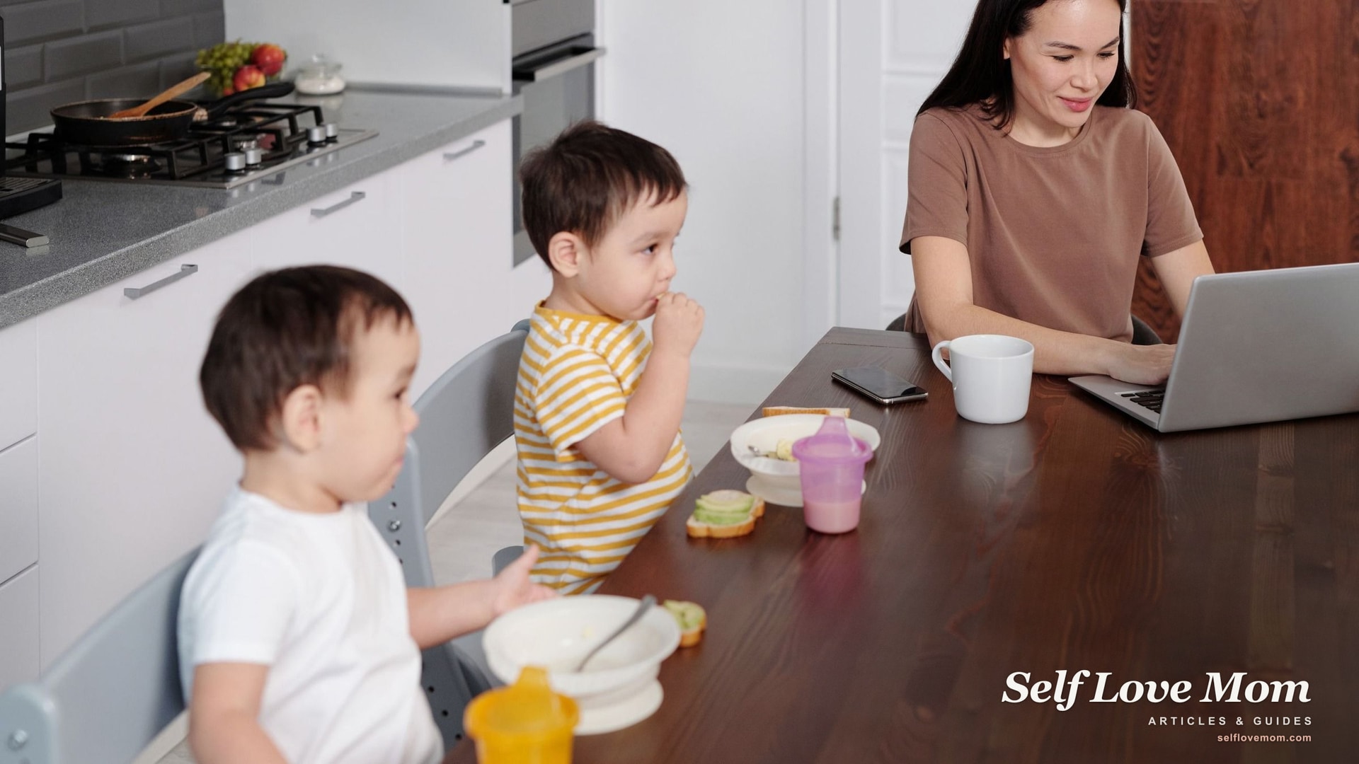 A busy mom works at a laptop while her two kids eat breakfast, the daily juggle the best gifts for busy moms help ease.