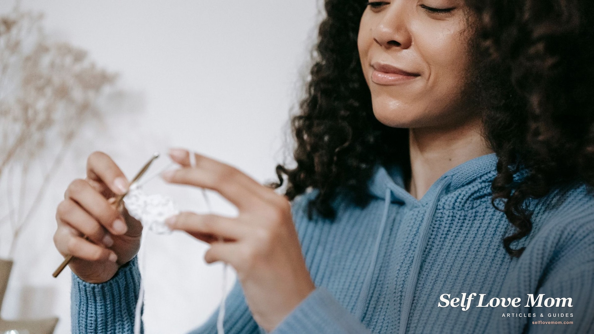 A woman smiles while crocheting at home, a hobby that costs little and can be put down the moment someone needs her.