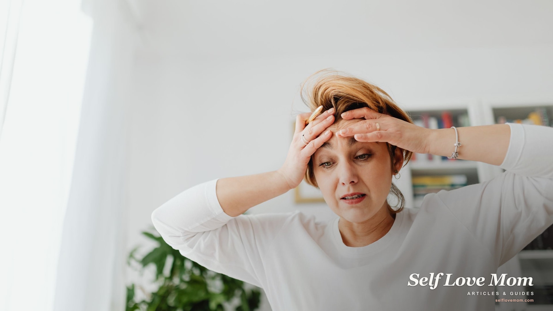 An exhausted mother holds her head in overwhelm at home, the kind of chronic stress that builds into burnout.