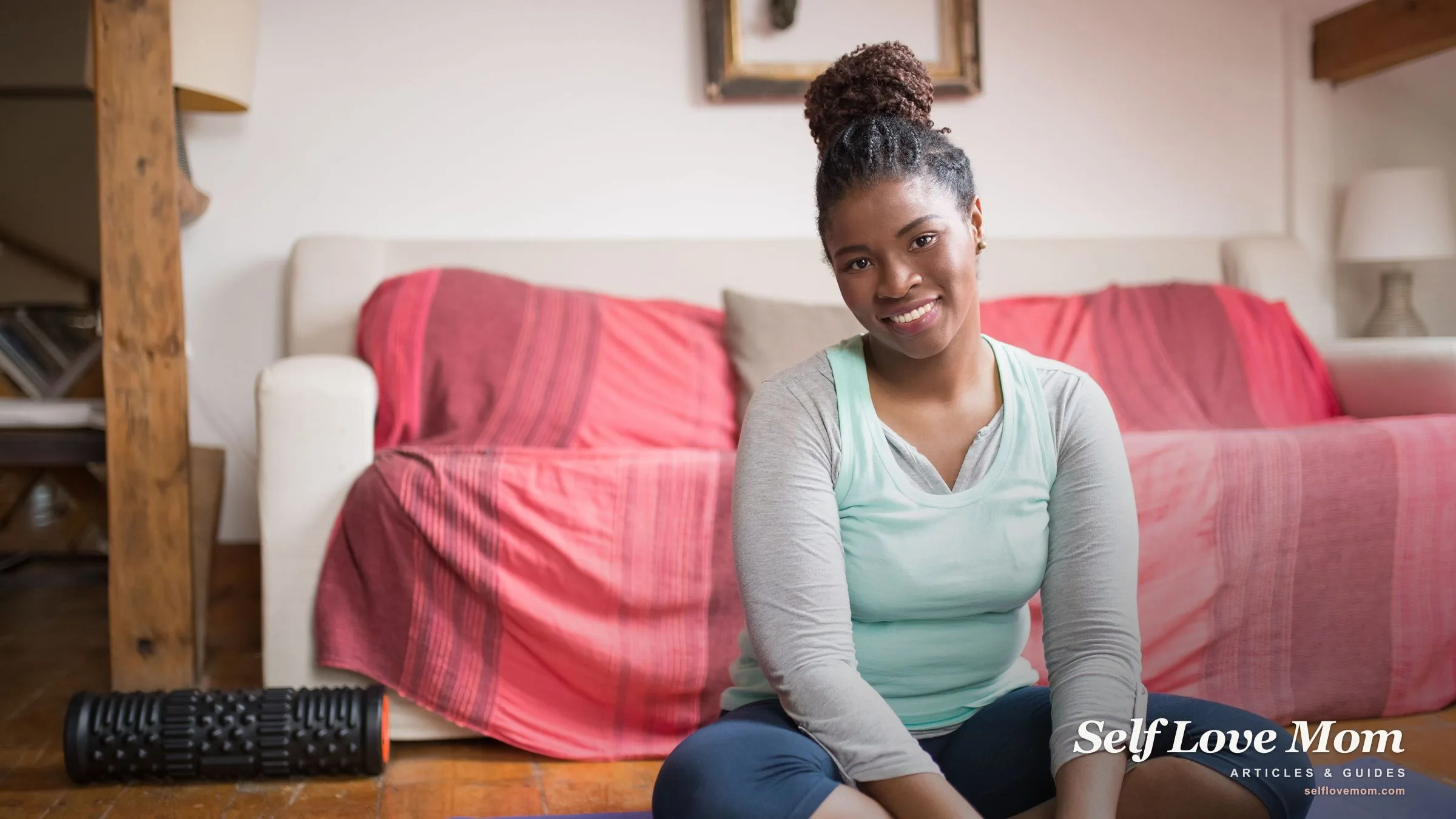A smiling mom sitting on a yoga mat in her living room after a free at-home workout, one way to do self care on a budget.