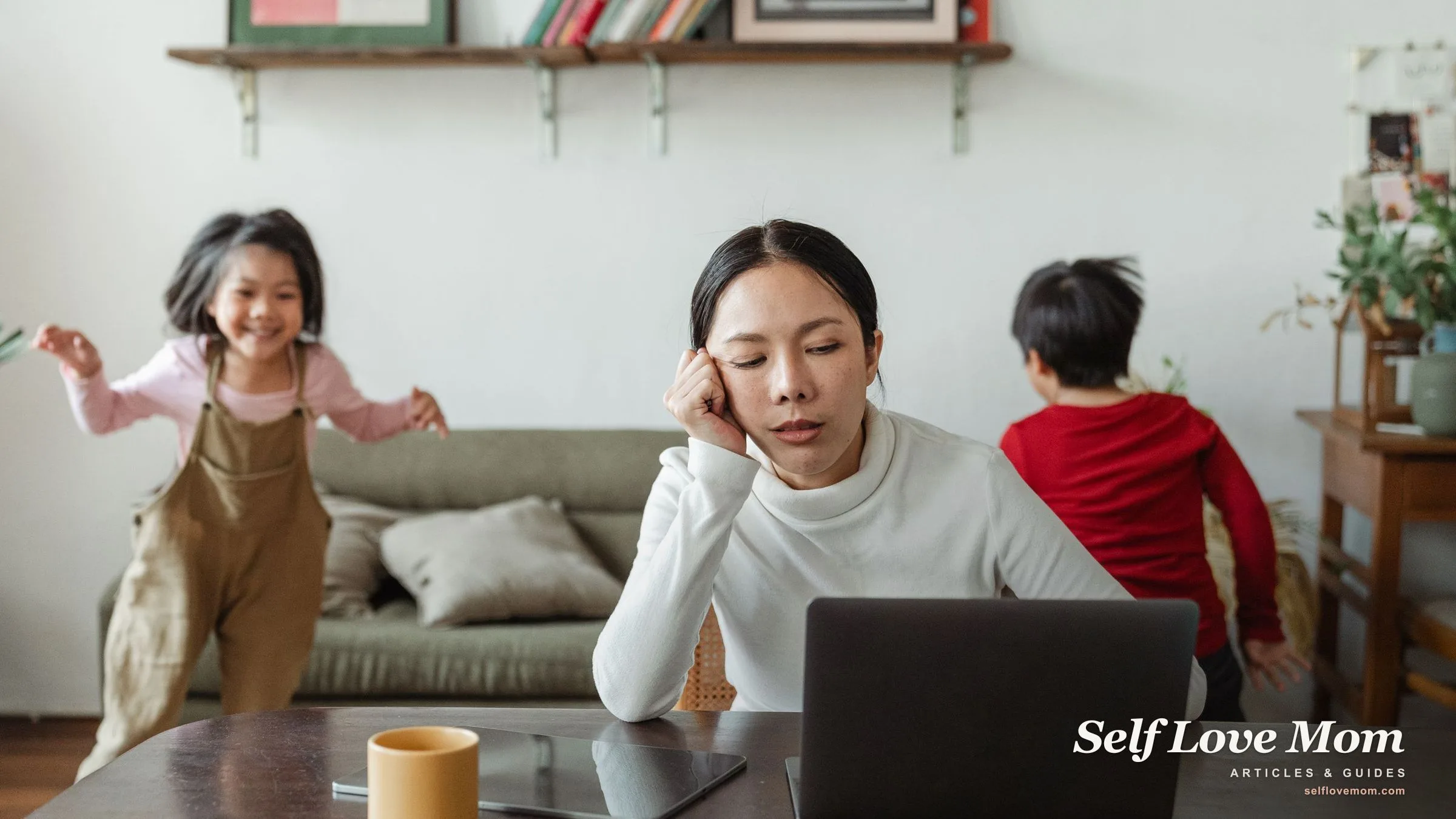 A working mom concentrates at her laptop while her two kids play behind her, the daily double shift that makes self care hard.