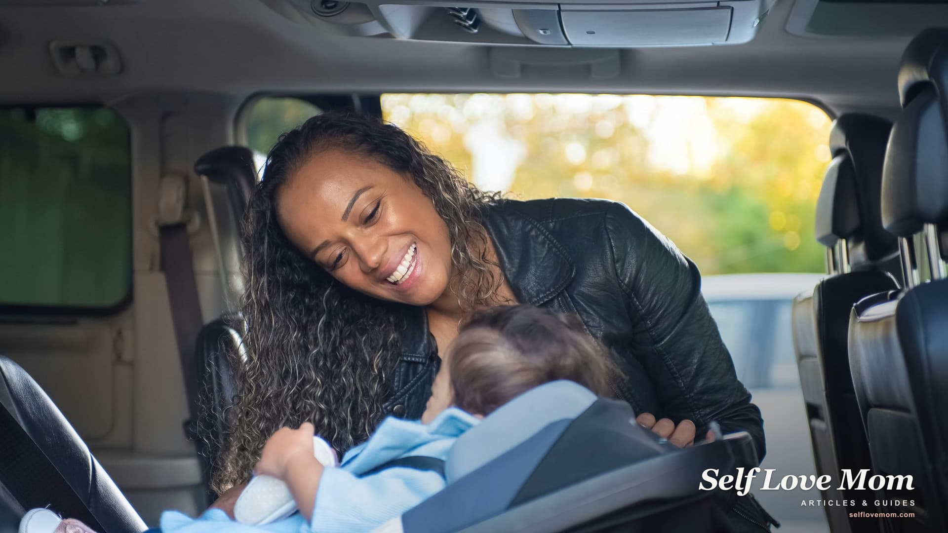 A smiling single mother leans into the back seat of her car to settle her baby into a car seat on a sunlit afternoon, the kind of reliable transportation single moms work to secure through car grant programs.