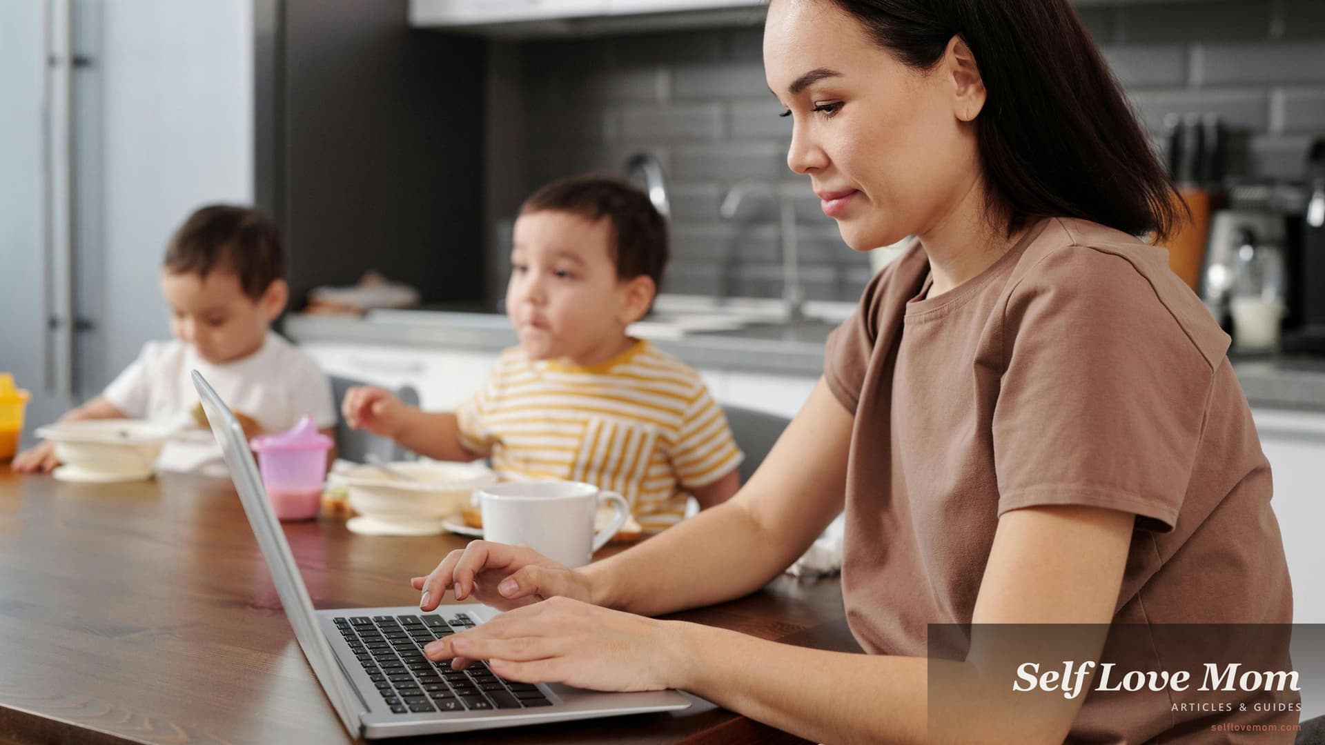 A single mom works on her laptop at the kitchen table while her kids eat breakfast, the everyday scene of applying for Illinois single-mom grants like TANF, SNAP, and the MAP Grant from home.