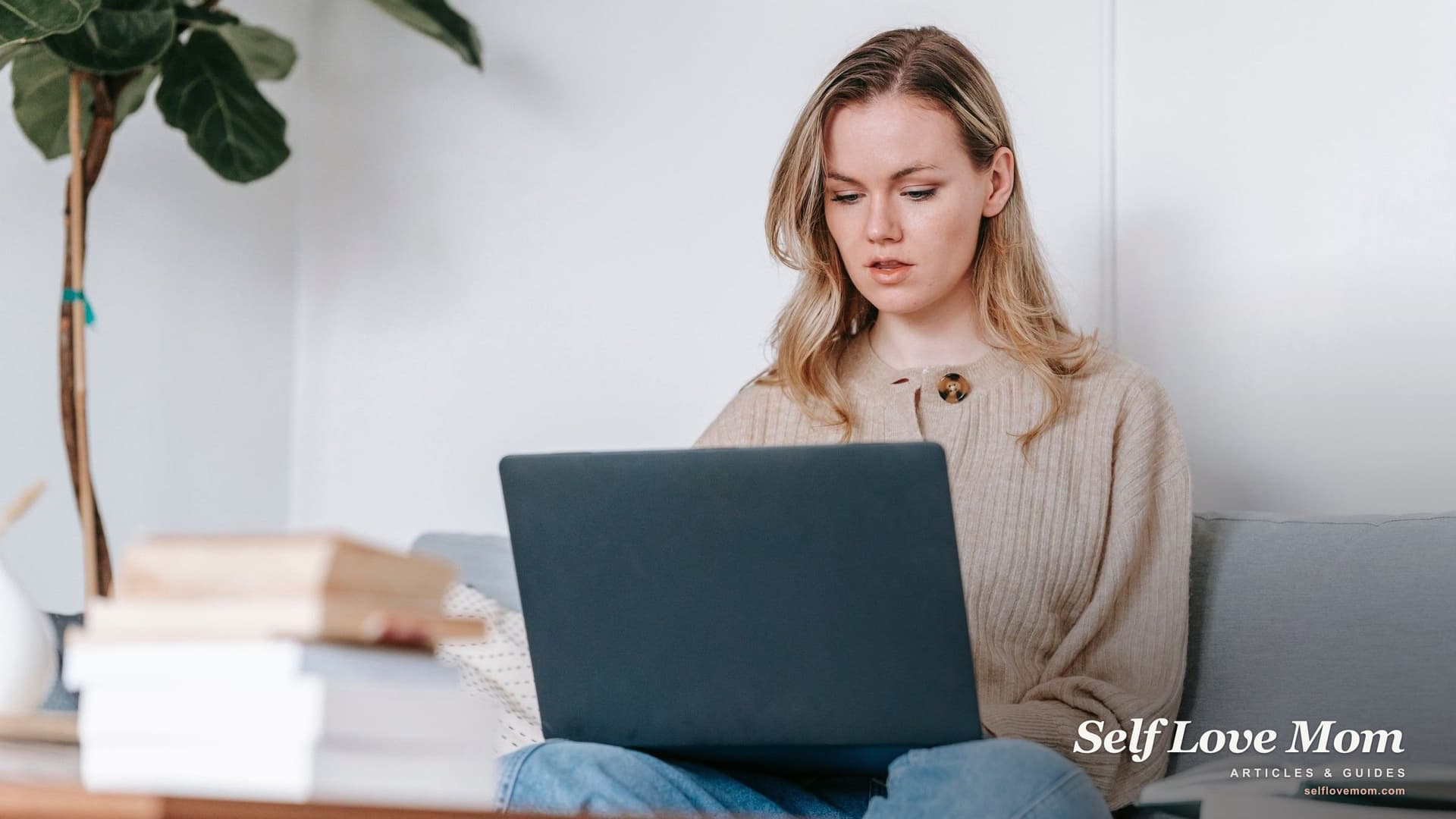 A woman studies on her laptop beside a stack of books at home, the kind of focus education grants for single moms are meant to fund.