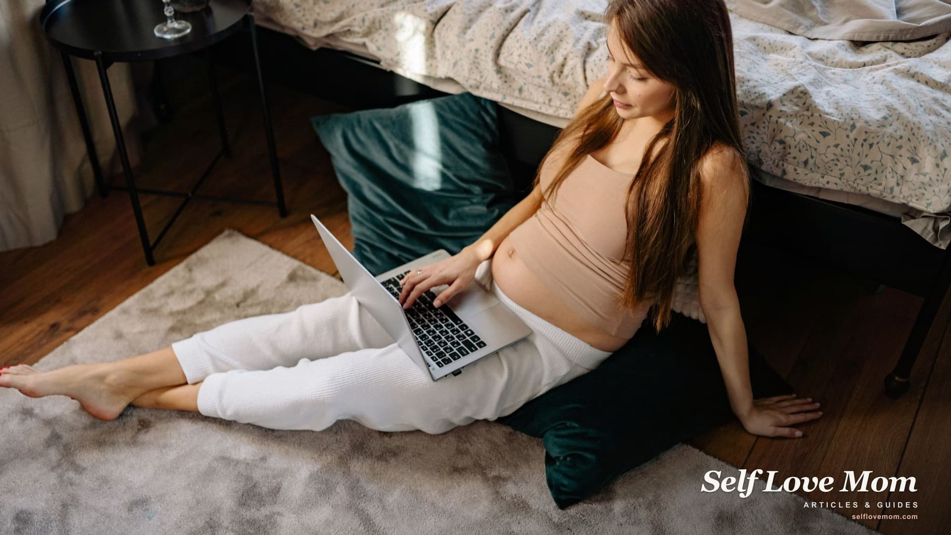 A pregnant woman sits at home with her laptop researching grants and financial help available to expecting moms in 2026.