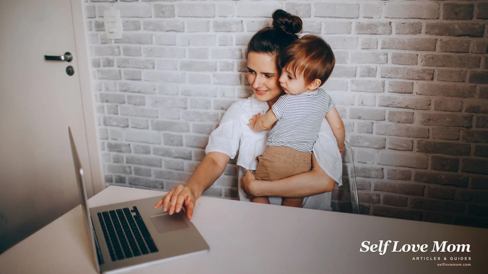 A single mom updates her resume on a laptop at home while holding her young child, returning to work.