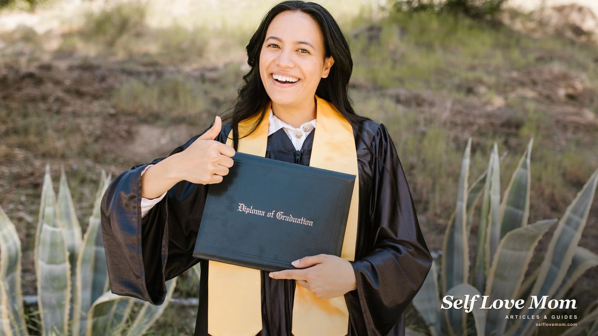 A smiling woman graduate in a cap and gown holds her diploma outdoors, the milestone scholarships for single moms help make possible.