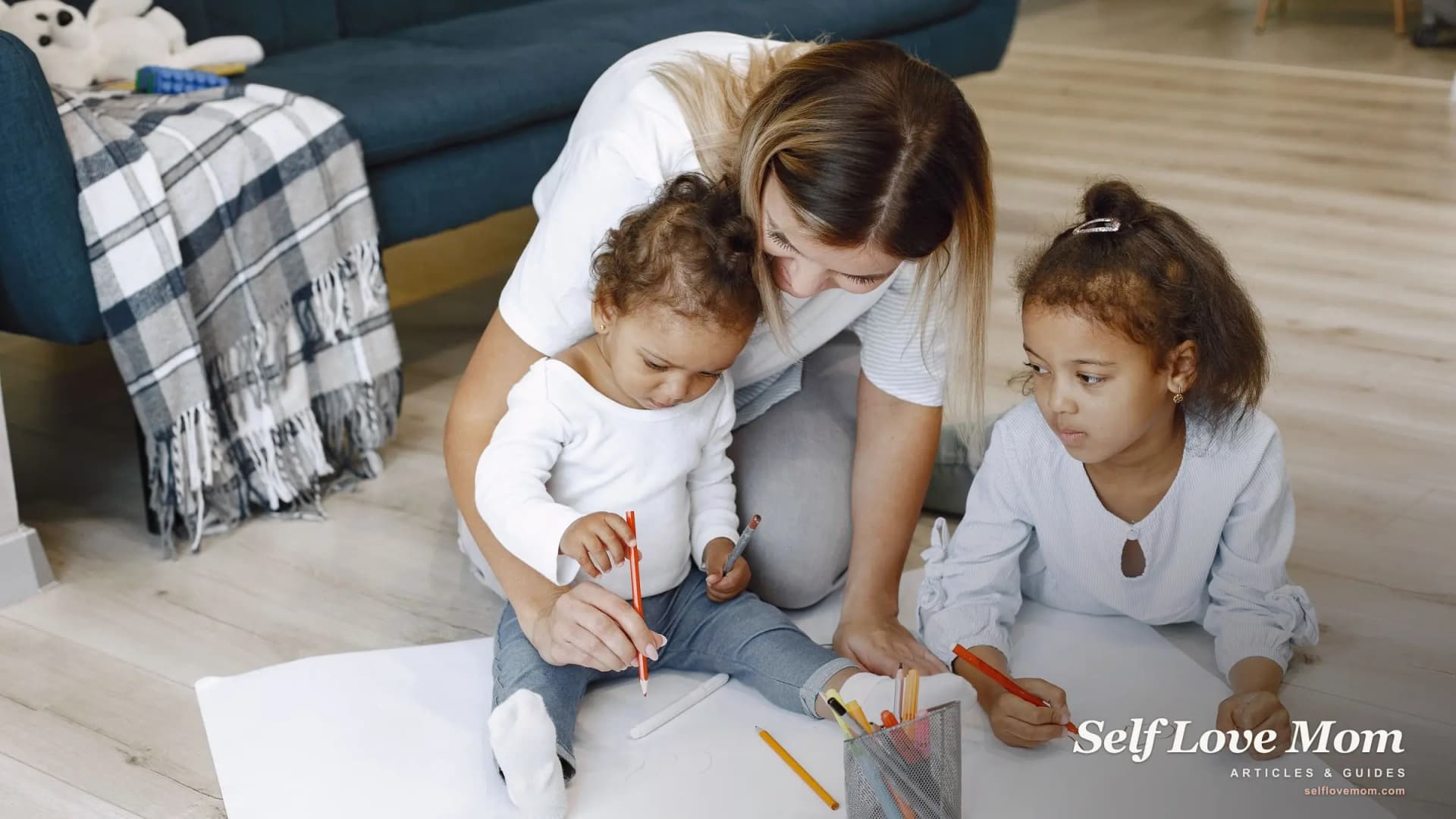 A stay-at-home mom draws on the floor with her two young children during a daily activity at home.