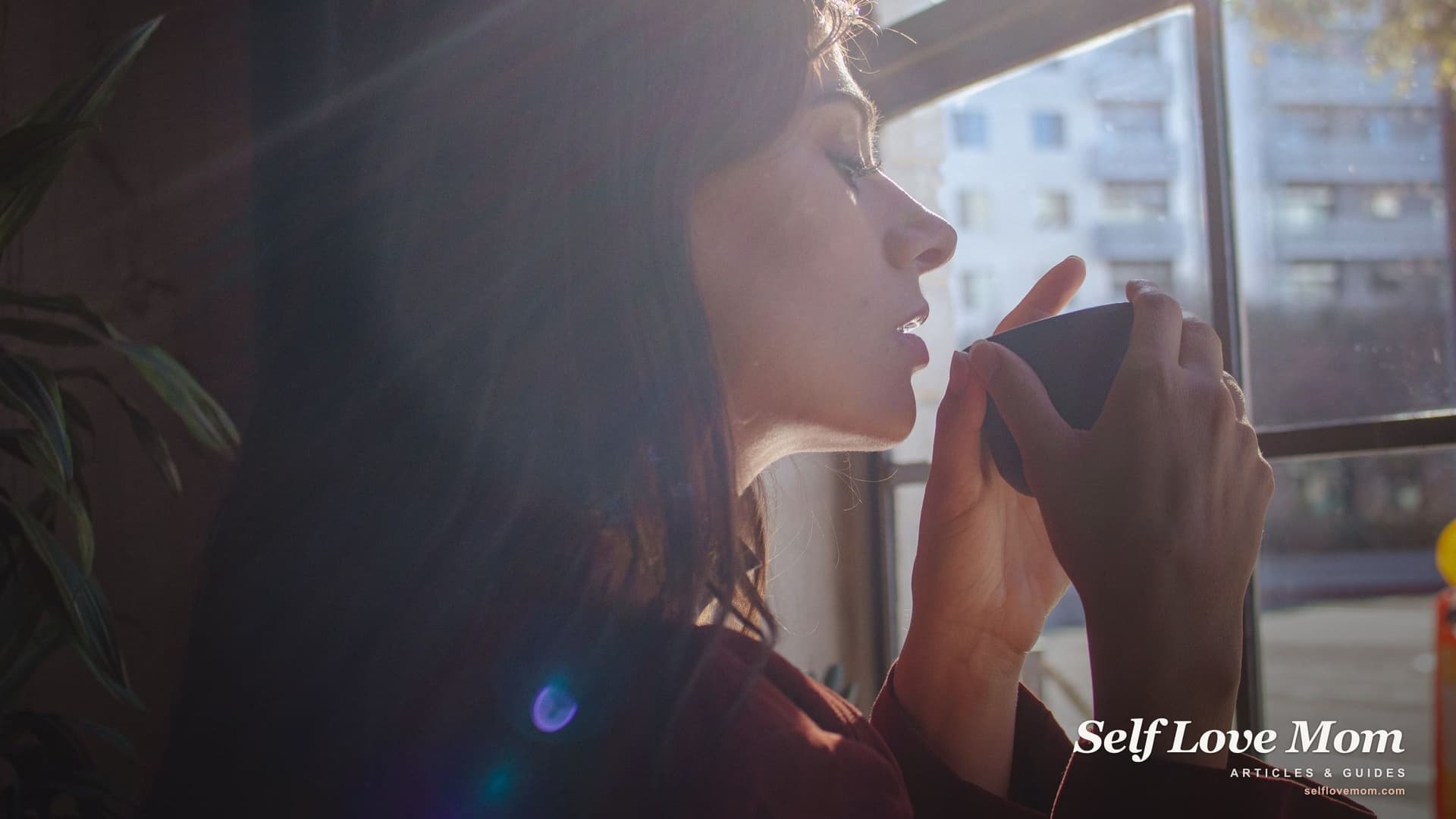 A single mother pauses with a warm drink by a sunlit window, a calm moment while seeking counseling and support.
