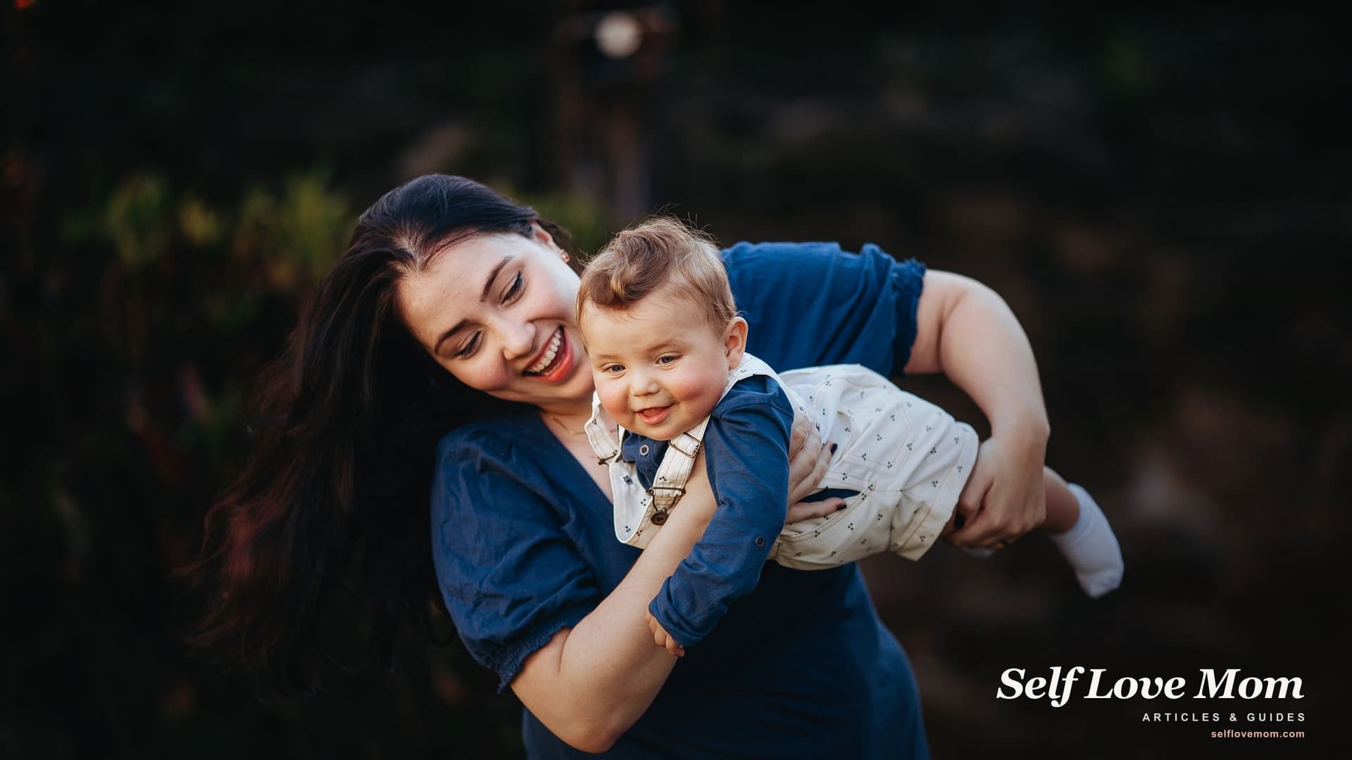 A smiling new mother holding her baby in warm light, a moment of self care for new moms who protect time to feel like themselves.