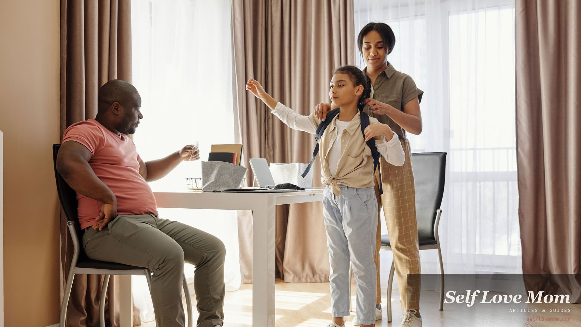 Two parents help their school age daughter into her backpack in a sunlit dining room before she leaves