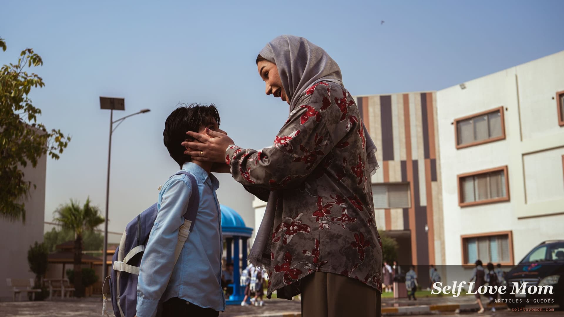 A mother says goodbye to her son outside school, backpack on, the everyday handover a shared schedule creates