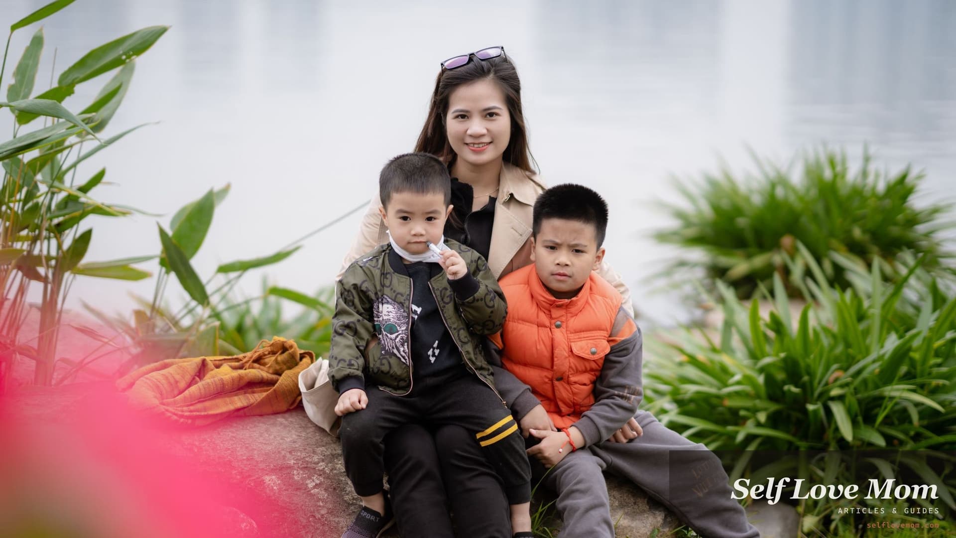 A mother sits beside a lake with her two young sons leaning into her, the kind of settled single household a parallel parenting plan is built to protect.