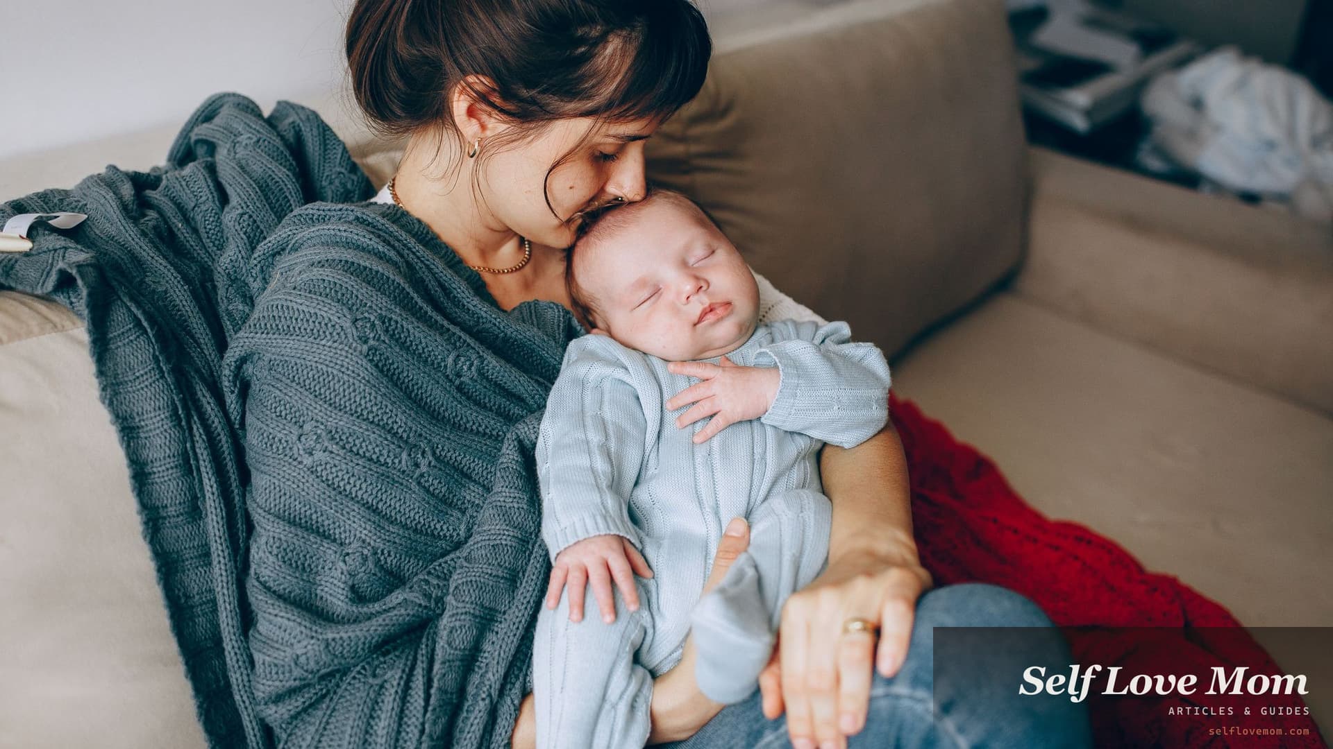 A mother rests her face against her sleeping newborn's head while sitting on a sofa with her eyes closed.
