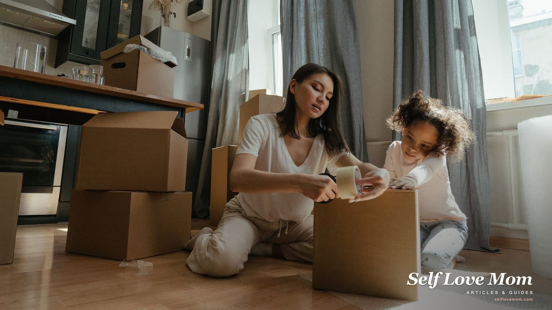 A mother and her young daughter sit on the bare floor of their new apartment taping moving boxes, with no sofa or table in the room yet.
