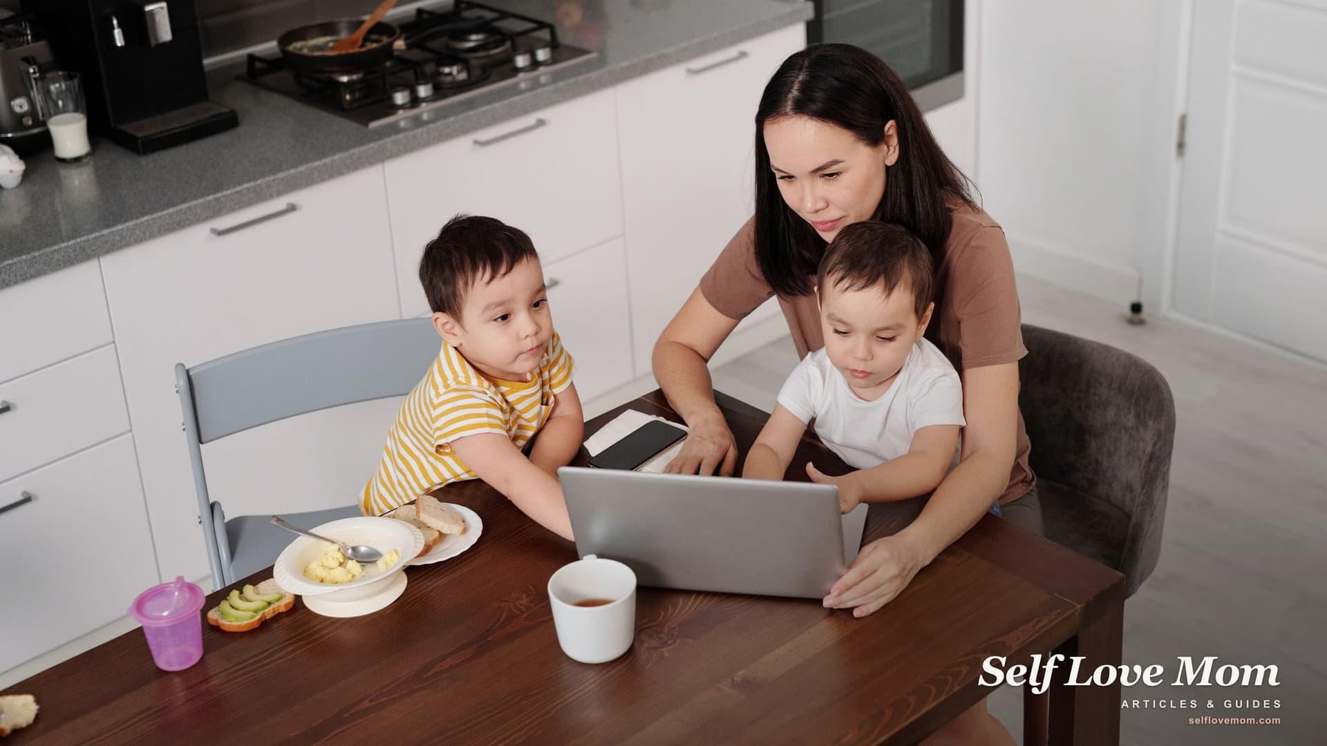 A single mother works through her tax return on a laptop at the kitchen table while her two young sons finish breakfast beside her.