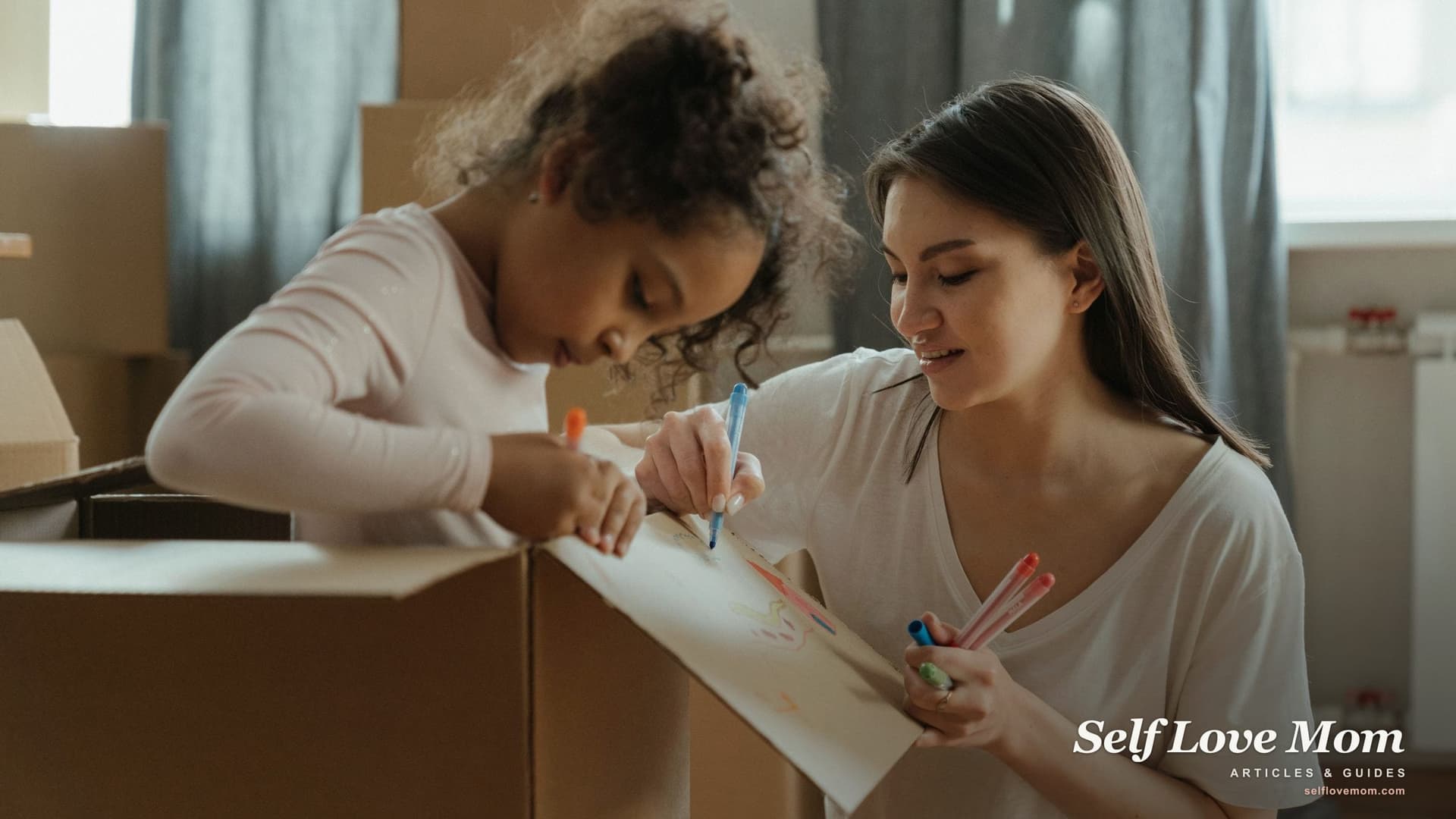 A first time home buyer single mom and her daughter draw on a moving box together, surrounded by packed cartons in their new home.