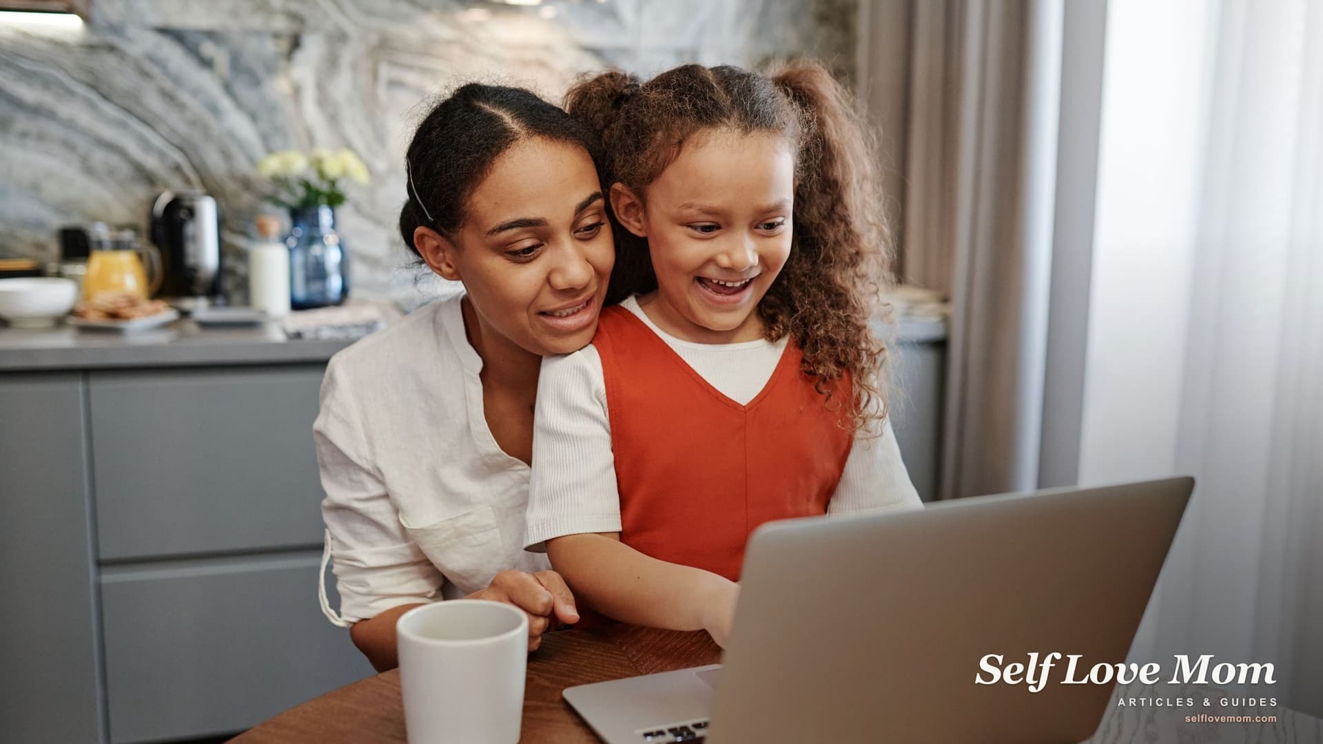 A single mom and her smiling daughter look at a laptop together at the kitchen table, the kind of place Georgia child support math often gets done.