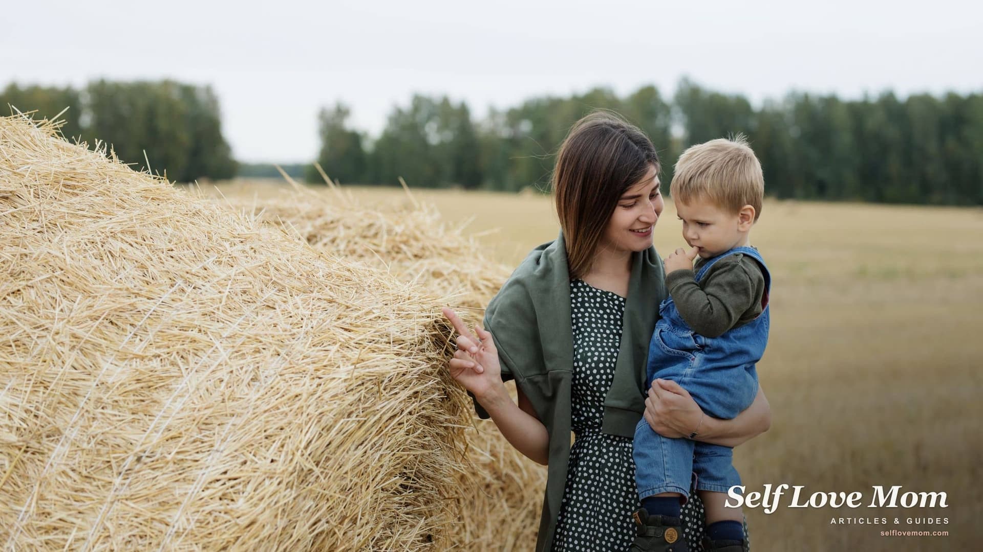 A single mom holds her young son beside a straw bale in a harvested field, the kind of farm-country family that grants for single mothers in Iowa are meant to help.
