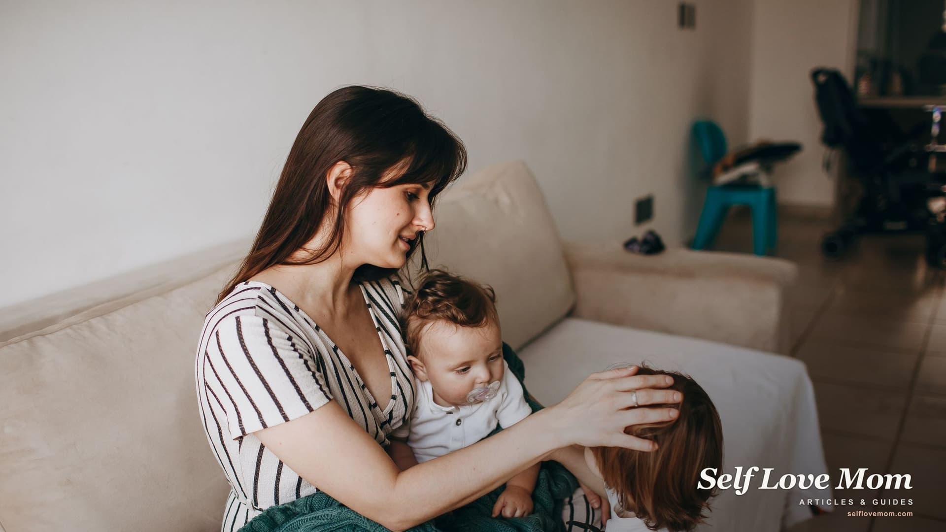 A single mother in Kentucky sits on the couch holding her baby and stroking her toddler's hair at home