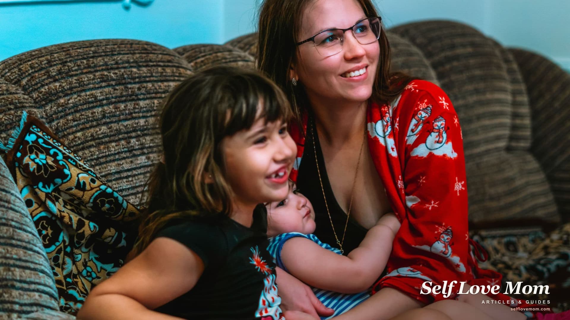 A single mom smiles on the couch with her young daughter and baby, the kind of stable rental that housing assistance for single mothers in Michigan can help keep.