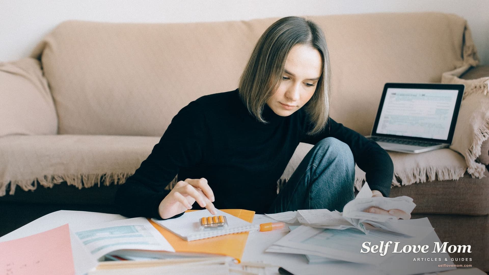 A mom sits on the living room floor totaling receipts on a calculator, her laptop open on the couch behind her, a home setup many single mothers use while learning how to become a bookkeeper.