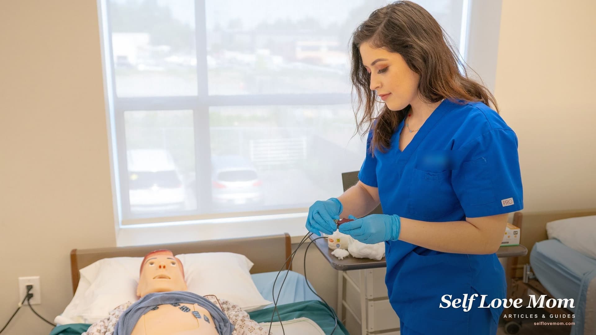 A nursing student in blue scrubs attaches heart monitor leads to a training manikin in a simulation lab, the kind of class that nursing scholarships for single mothers help pay for.