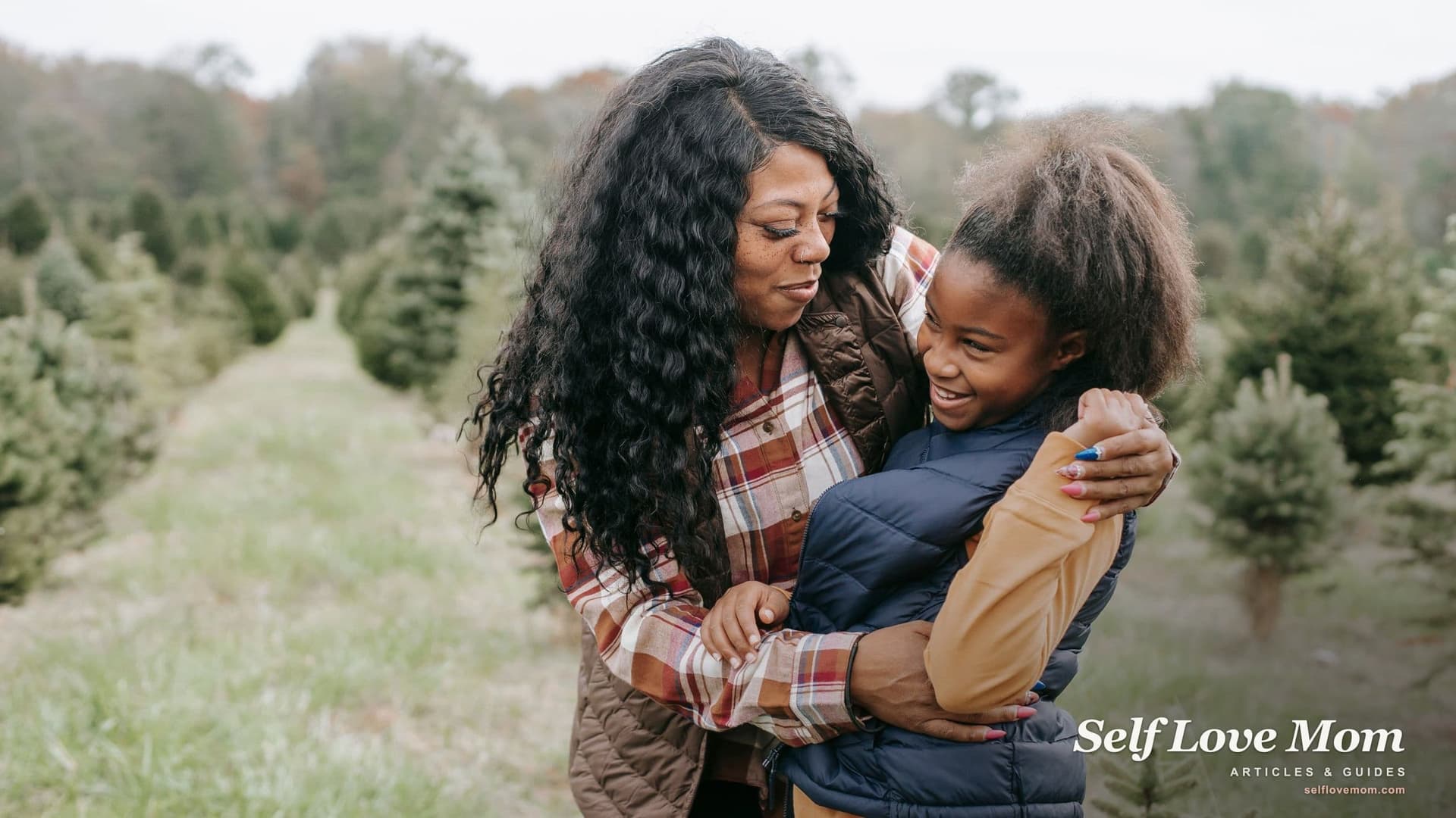 A mother hugs her laughing daughter outdoors among young trees, the kind of family a single woman builds through adoption.