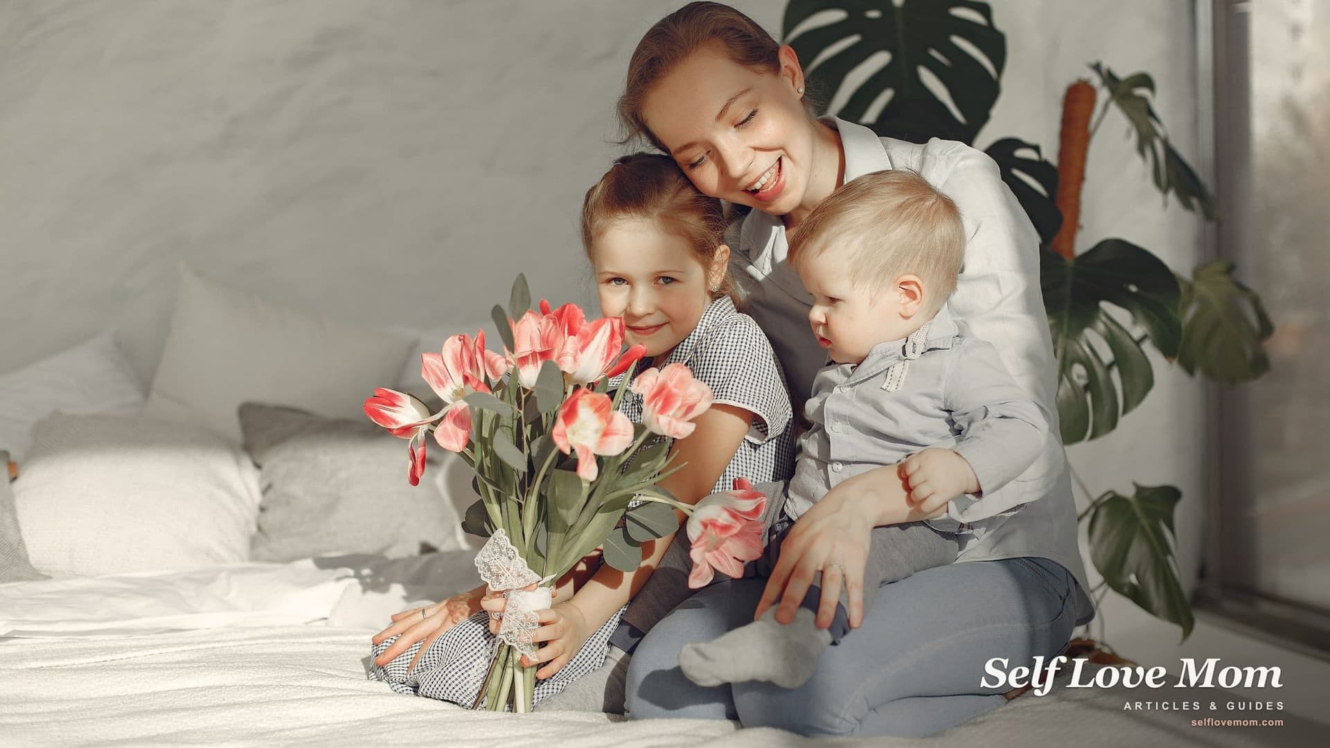 A smiling mother sits on a bed with her baby son on her lap while her young daughter holds pink tulips, the household a single mom has in mind when she asks for custody.