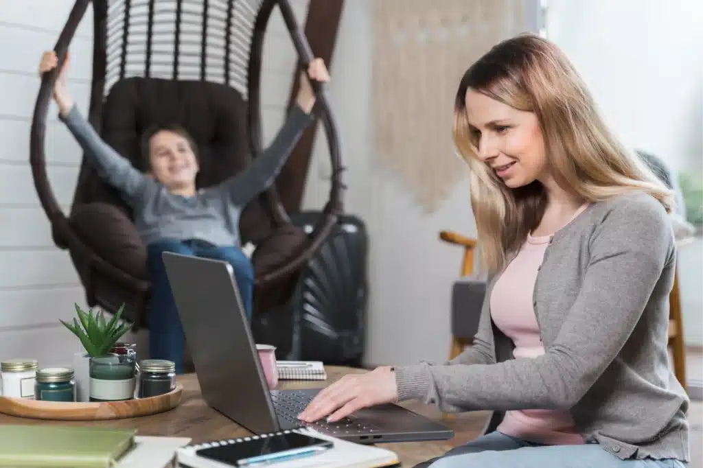 Single mom working from home on her laptop while her child plays, representing the best careers for single moms