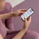 A woman doing yoga and using free self care apps on her phone, enhancing her fitness and wellness journey.