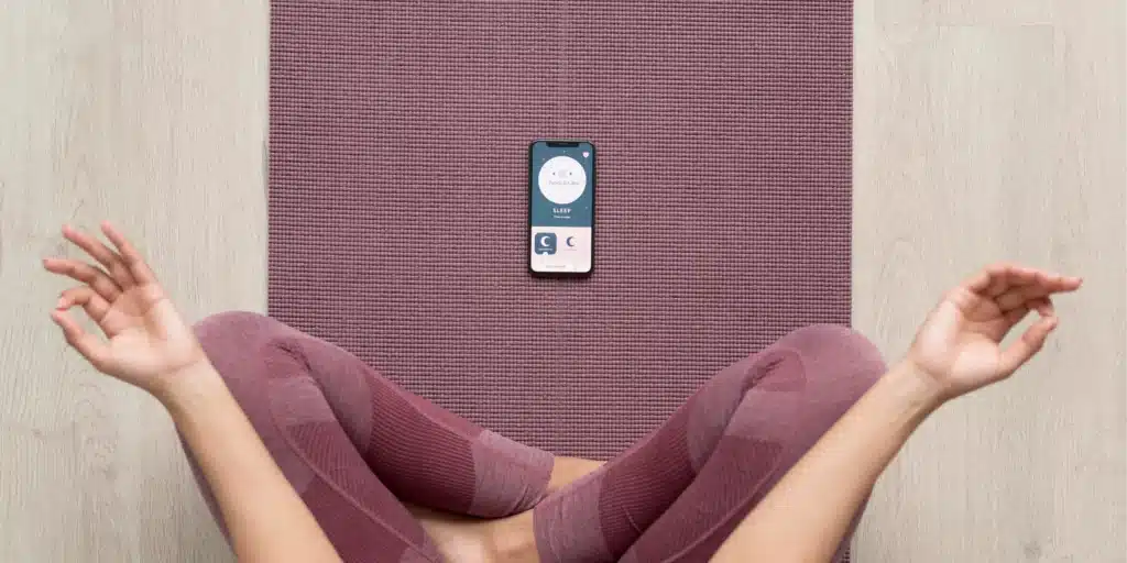 A mom doing yoga with free self care apps on her phone, offering features like "Peace & Calm" and "Sleep" for mindfulness and stress relief.