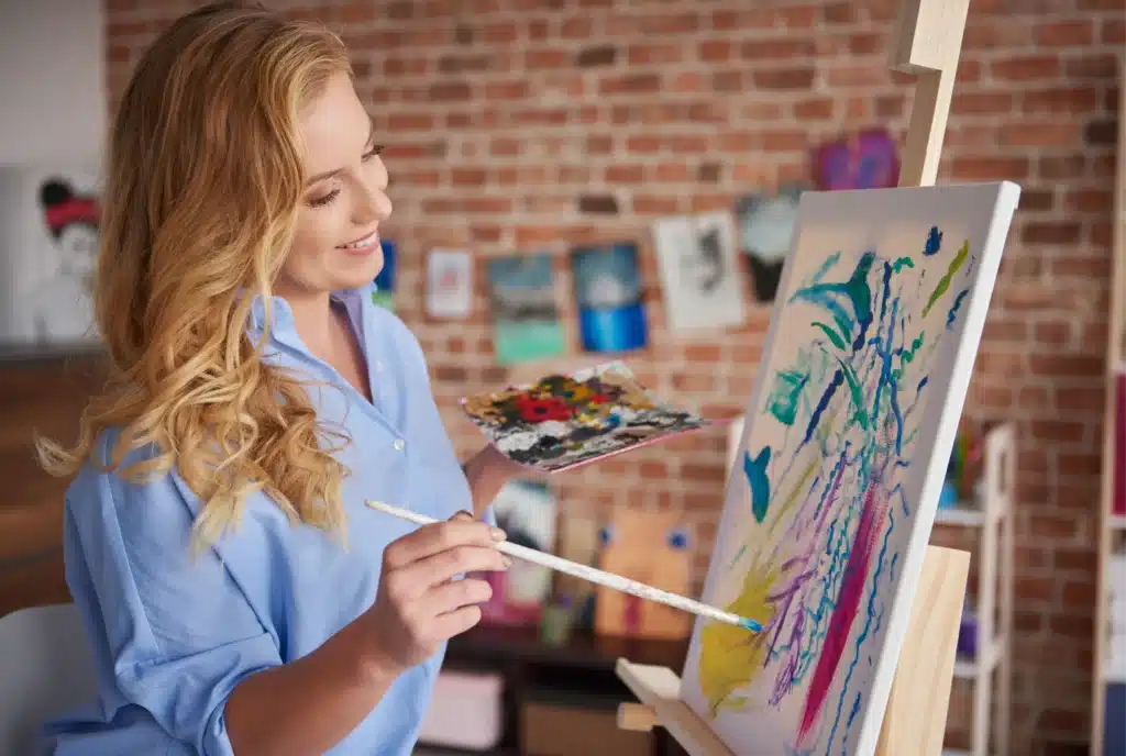 A stay-at-home mom enjoying one of the creative hobbies for stay at home moms, painting a beautiful canvas with vibrant colors in her creative space.