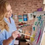 A stay-at-home mom enjoying one of the creative hobbies for stay at home moms, painting a beautiful canvas with vibrant colors in her creative space.