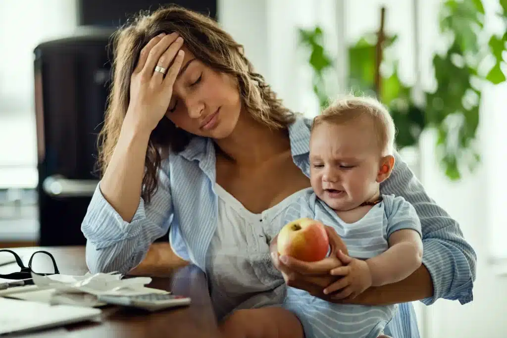 Tired mother holding baby and feeling overwhelmed, showing common signs of mom burnout such as stress and fatigue