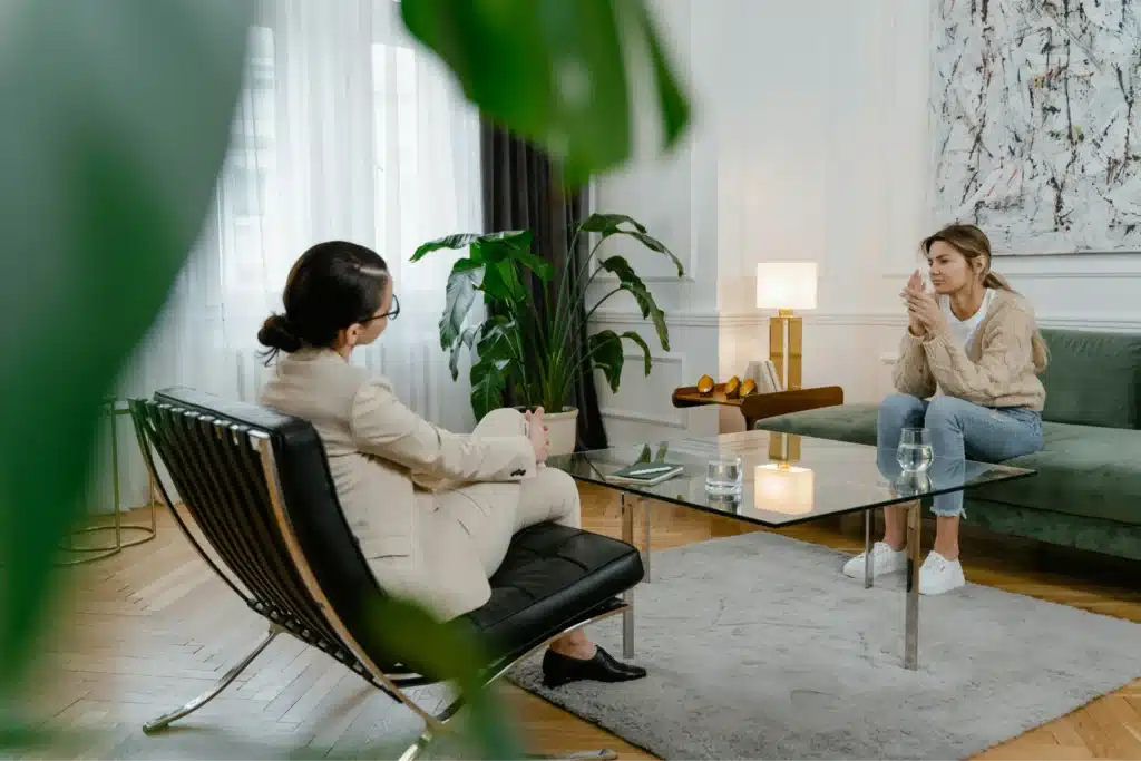 A single mother talks with a therapist in a modern office, sitting on a green couch with a thoughtful expression, highlighting the emotional challenges faced by single parents.